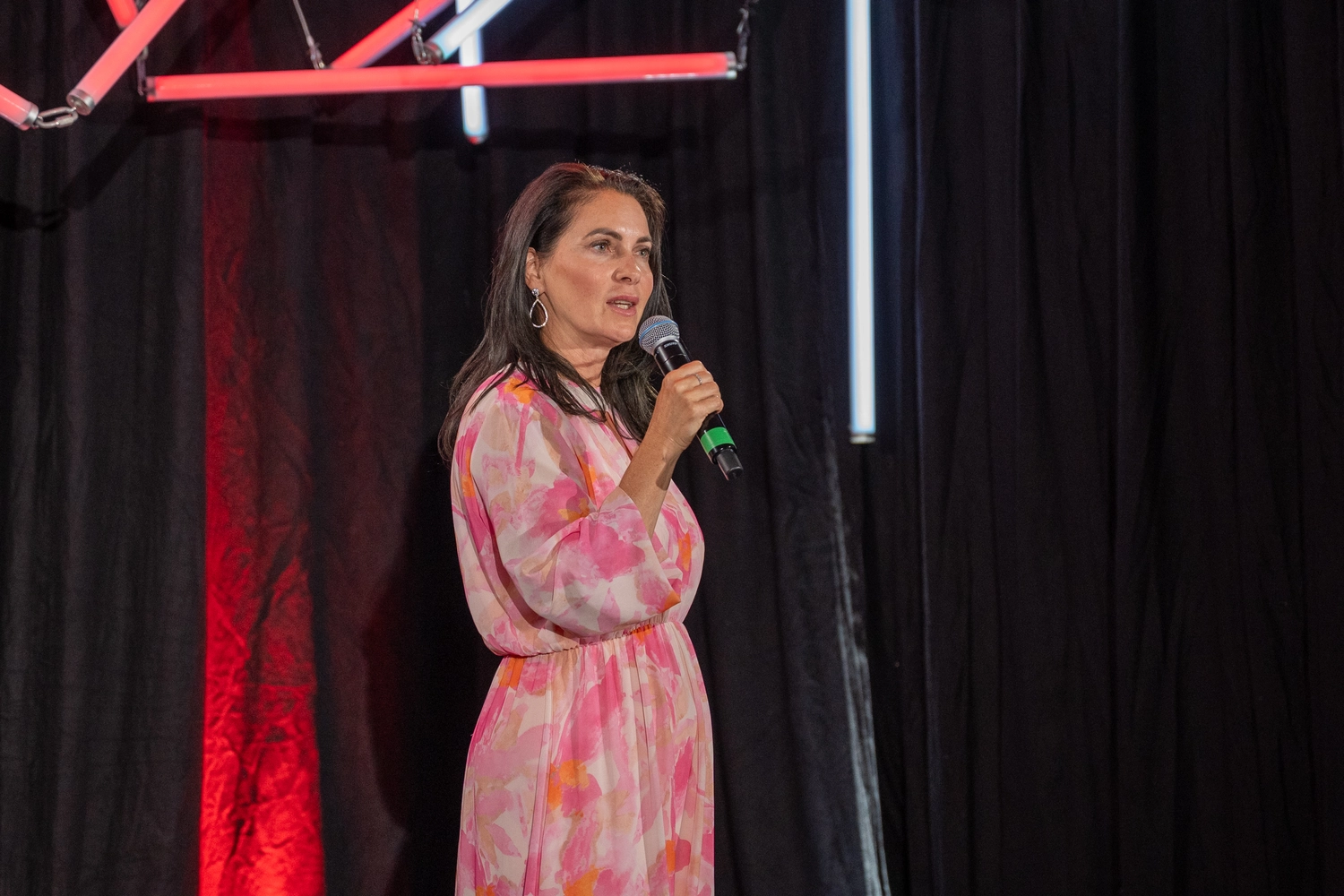 Kathrin Ipse - Expertin für Stressregulation, Nervensystem-Balance und professionelle Hypnose - Eine Frau in einem rosa-weiß gemusterten Kleid spricht auf einer Bühne in ein Mikrofon.