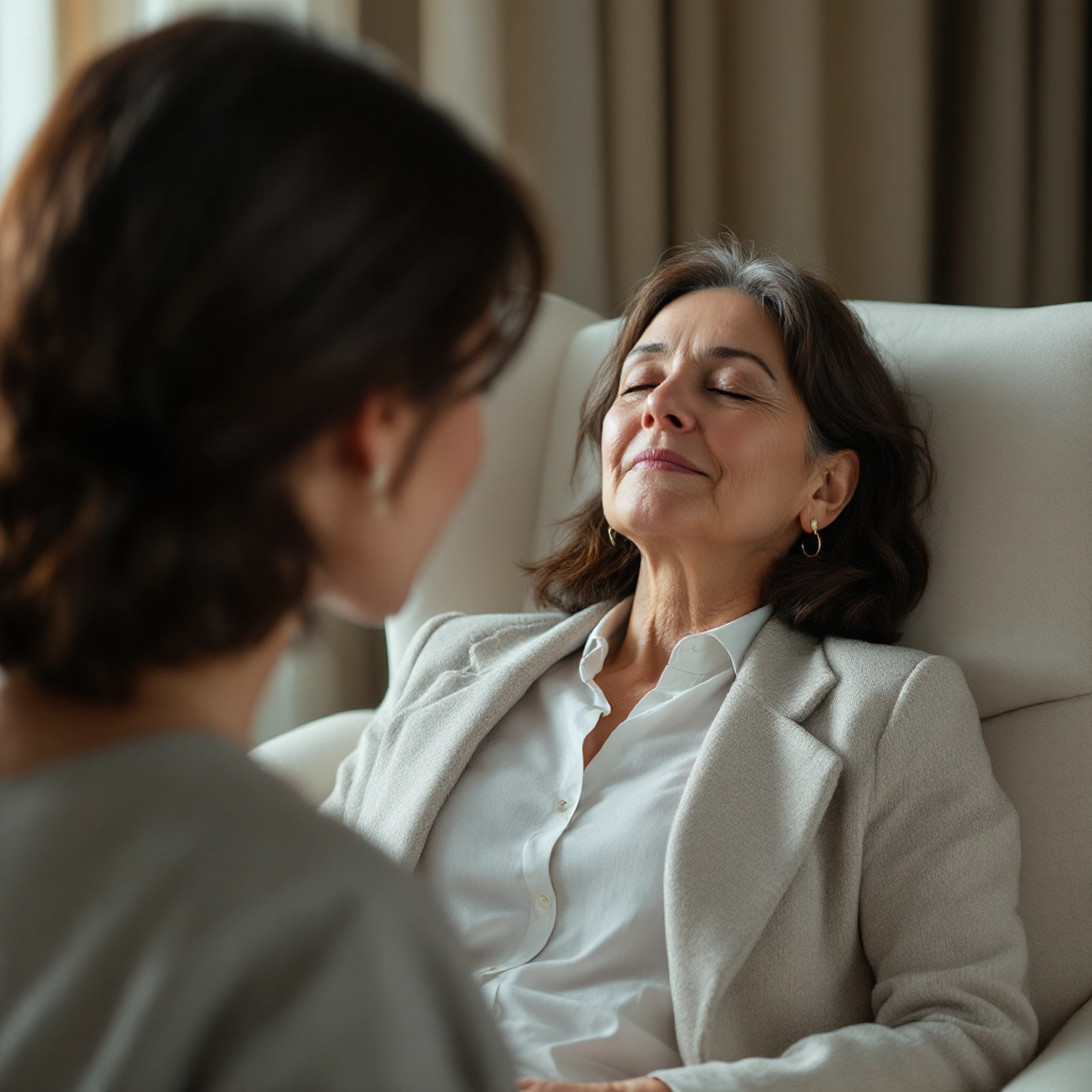 Kathrin Ipse - Expertin für Stressregulation, Nervensystem-Balance und professionelle Hypnose - Eine Frau liegt mit geschlossenen Augen auf einem Stuhl, während ihr eine Therapeutin gegenübersitzt.